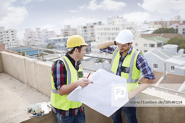 Construction worker and engineer reviewing blueprints at highrise construction site