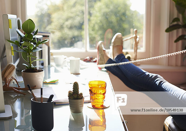 Frau am Telefon mit erhobenen Füßen auf dem Schreibtisch im sonnigen Home-Office