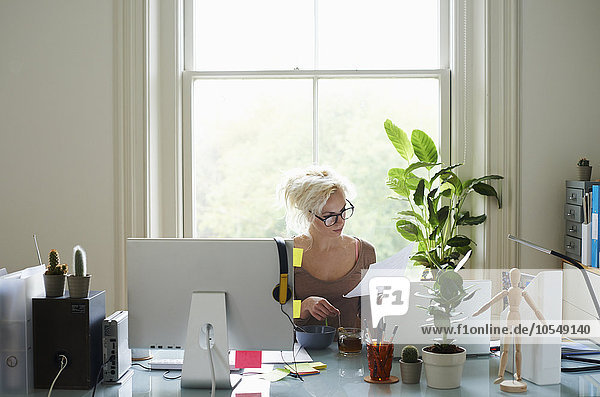 Junge Frau liest Papierkram am Schreibtisch im Home-Office