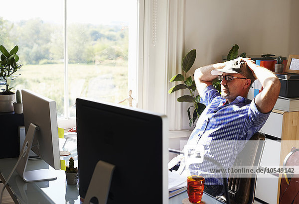 Zurücklehnender Mann bei der Arbeit am Computer im sonnigen Home-Office
