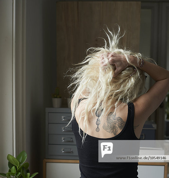 Junge Frau mit den Händen in den Haaren  die Rücken-Tattoos enthüllen