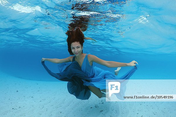 Eine junge schöne Frau in einem blauen Kleid schwimmt unter Wasser  über dem sandigen Meeresboden  Indischer Ozean  Malediven  Asien