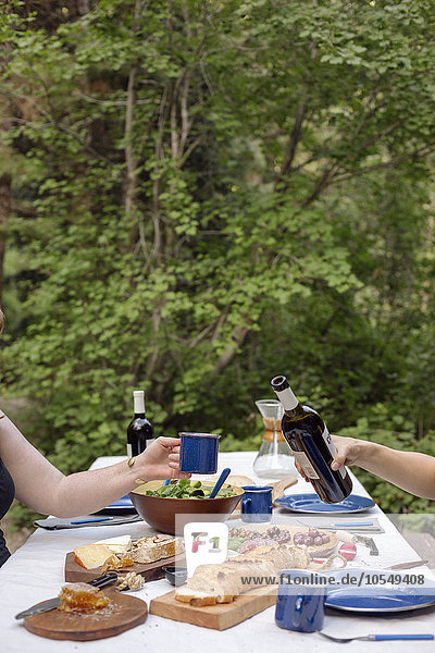 Tisch in einem mit Tellern und Speisen gedeckten Garten  ein Mann schenkt ein Glas Wein ein.