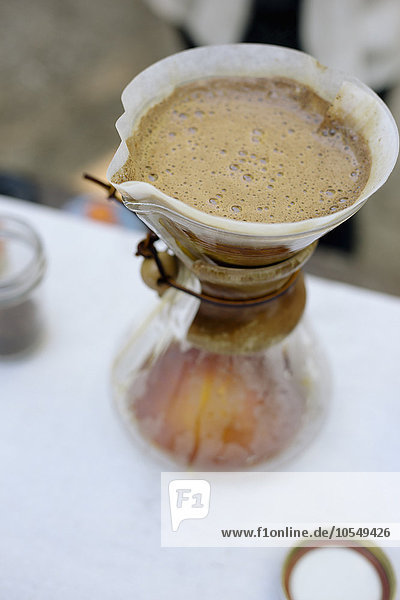 Hochwinkelansicht einer Glas-Kaffeemaschine und Filterpapier mit Kaffee- und Wasserfilterung durch