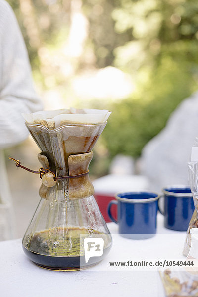 Nahaufnahme einer gläsernen Kaffeemaschine auf einem Tisch in einem Garten.
