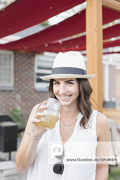 Lächelnde Frau  die in einem Garten steht und ein Getränk in der Hand hält.
