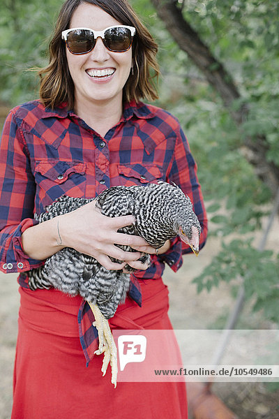 Porträt einer lächelnden Frau  die eine grau gesprenkelte Henne hält.