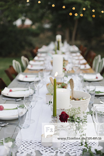 Langer  mit Tellern und Gläsern gedeckter Tisch  Essen und Trinken in einem Garten.