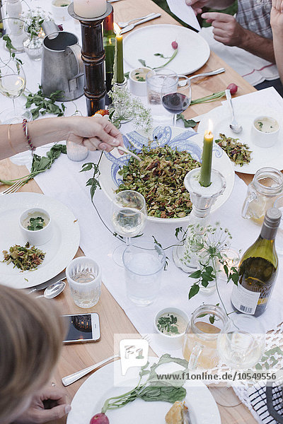 Menschen um einen Tisch bei einer Gartenparty  eine Schüssel Salat.