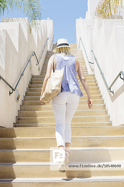 Blonde Frau mit Hut  die eine Treppe hinaufgeht.
