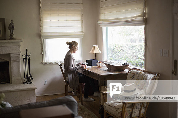Blonde Frau  die an einem Schreibtisch am Fenster sitzt und sich Fotos ansieht.