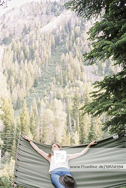 Woman relaxing in a large hammock in a forest.