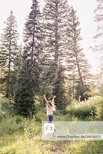 Frau springt vor Freude in einem sonnenbeschienenen Wald.