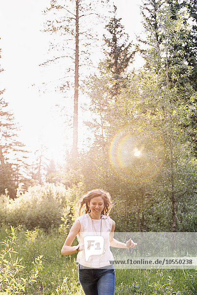 Smiling woman running through a sunlit forest.