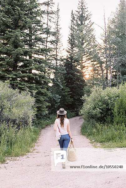 Frau  die auf einem Waldweg geht und eine Tasche trägt.