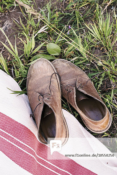 High angle view of a pair of worn brown leather lace up shoes on a picnic blanket.