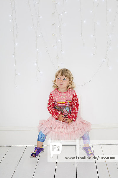 Junges Mädchen sitzt auf einem Stuhl in einem Fotografenstudio und posiert für ein Bild.