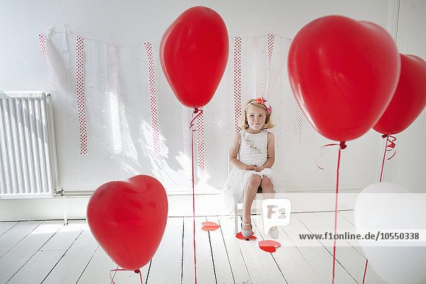 Young girl posing for a picture in a photographers studio  surrounded by red balloons.