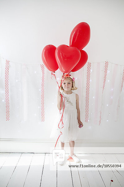 Young girl posing for a picture in a photographers studio  holding red balloons.