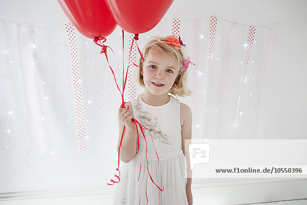 Young girl posing for a picture in a photographers studio  holding red balloons.