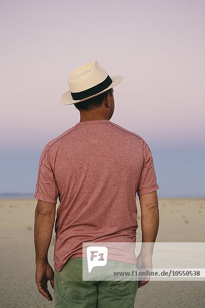 Ein Mann mit einem Strohhut  der in der Morgendämmerung in der Wüste inne hält  um die Landschaft der Playa zu betrachten.