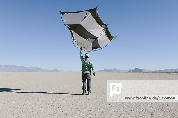 Mann  der im offenen Raum der Wüste ein Zelt mit Kapselkapseln über seinem Kopf hält.