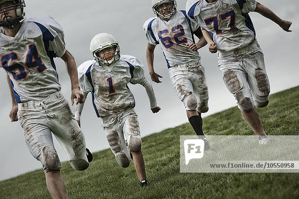 Eine Gruppe von vier Fussballspielern  Jugendliche in Sportuniform und mit Schutzhelmen laufen vorwärts.