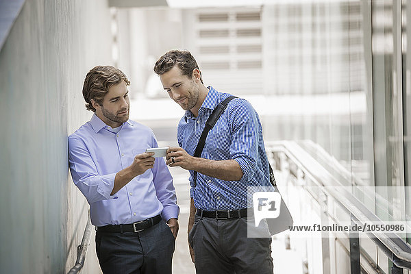 Two businessmen standing in an urban street  using smart phones.