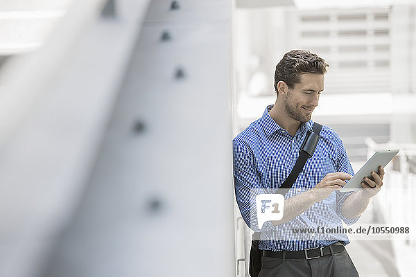 Ein Mann in Hemd und Krawatte  der ein digitales Handheld-Tablett in einer städtischen Szene benutzt.