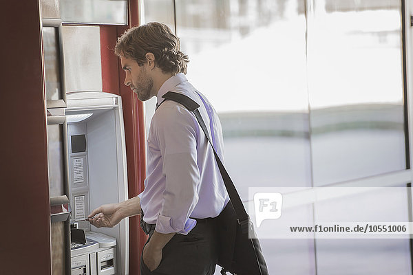 A man with a laptop bag using an ATM  a cash machine on a city street.