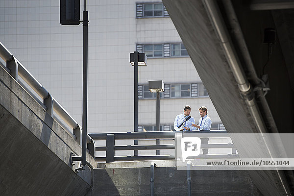 Zwei an ein Geländer gelehnte Geschäftsleute stehen auf einem Stadtgang  Blick von unten.
