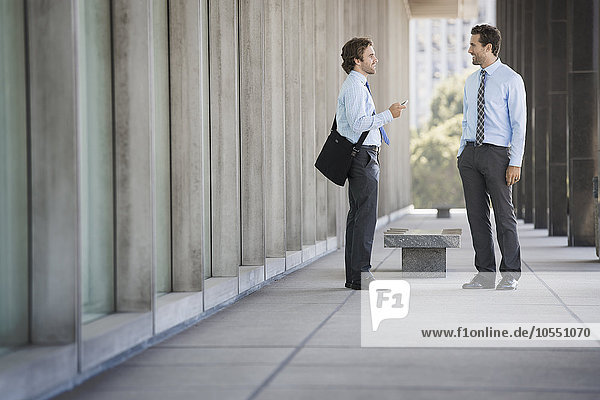 Two businessmen on a walkway outside a building  talking.