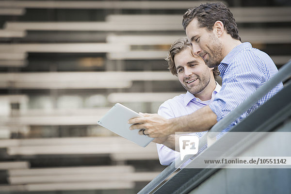 Zwei Männer auf einem städtischen Gehweg  die auf ein digitales Tablet schauen.