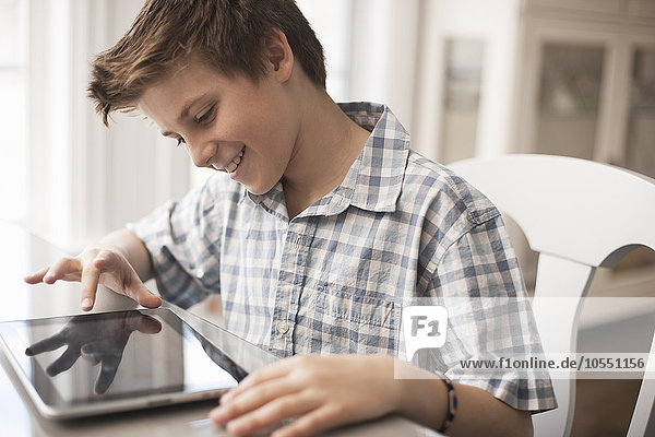 A boy seated at a table using a digital tablet  hand on the touch screen.