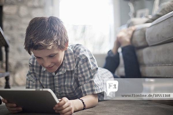 Ein Junge liegt vorne auf dem Boden und schaut auf ein digitales Tablett.