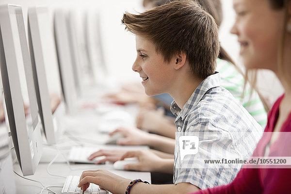 Eine Gruppe von Jugendlichen  Jungen und Mädchen  die im Unterricht an Computerbildschirmen arbeiten.
