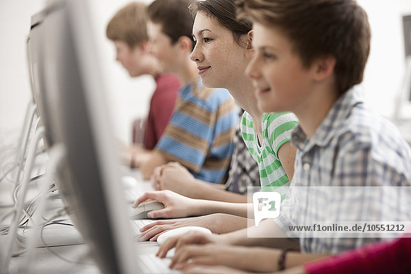 Eine Gruppe von Jugendlichen  Jungen und Mädchen  die im Unterricht an Computerbildschirmen arbeiten.