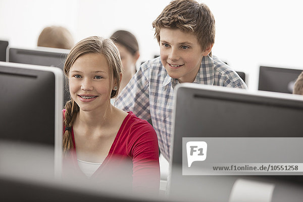 Ein Computer-Laborraum der Schule  mit Reihen von Bildschirmen. Zwei junge Leute schauen aufmerksam auf den Bildschirm.