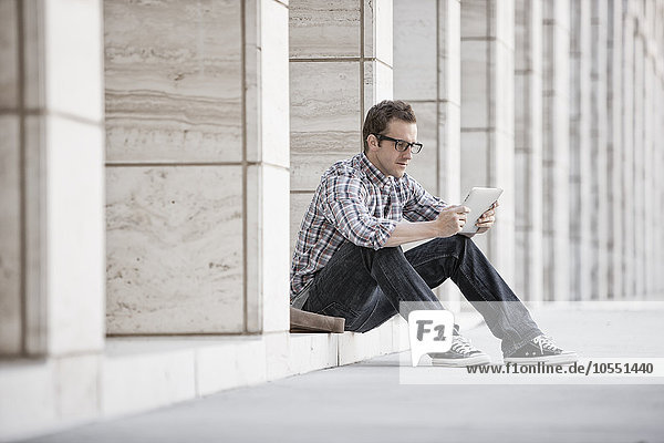 Ein Mann  der sich entspannt und sein Telefon überprüft  sitzt vor einem Gebäude.