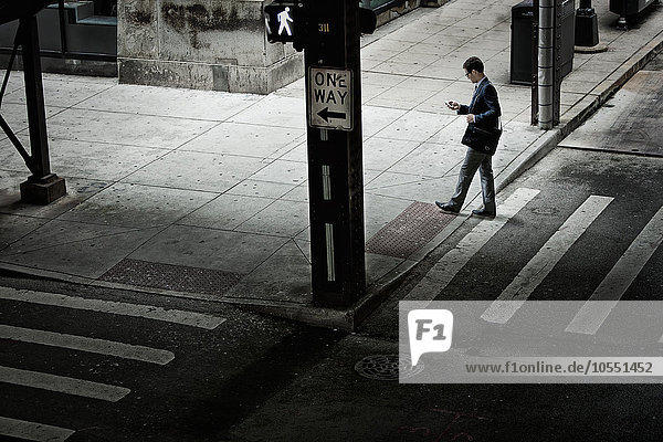 Ein Mann geht über eine Straßenkreuzung und schaut auf ein Telefon in der Hand.