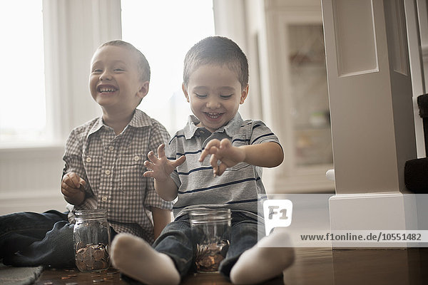 Two children playing with coins  dropping them into glass jars.