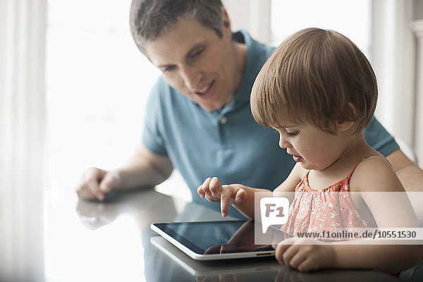 Ein Mann und ein kleines Kind sitzen  schauen auf ein digitales Tablett und berühren den Bildschirm.