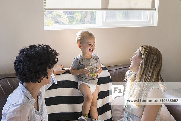 Caucasian lesbian mothers laughing with baby son on sofa
