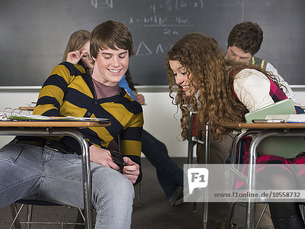 Schüler benutzen Mobiltelefon am Schreibtisch im Klassenzimmer