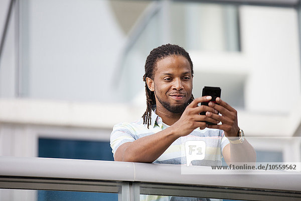 Afroamerikanischer Geschäftsmann benutzt Mobiltelefon auf Balkon