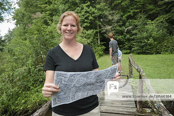 Kaukasische Frau liest auf einem Steg im Wald eine Karte