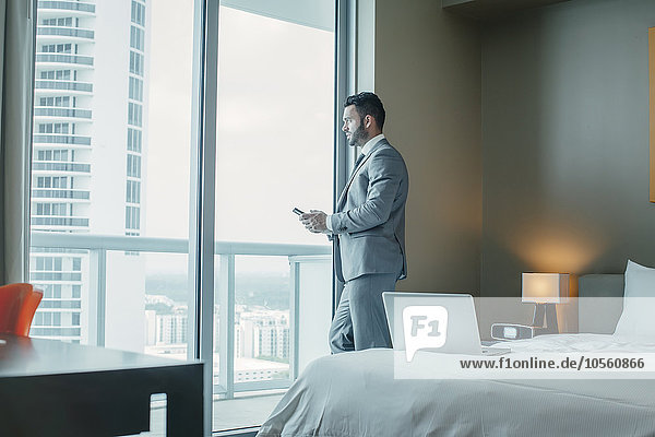 Businessman using cell phone at hotel window