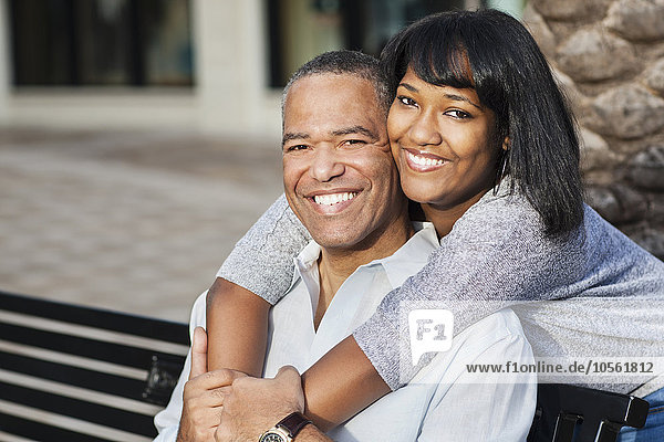 Afroamerikanischer Vater und Tochter umarmen sich auf einer Bank