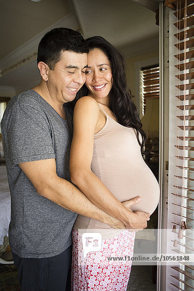 Hispanischer Mann umarmt den Bauch seiner schwangeren Frau