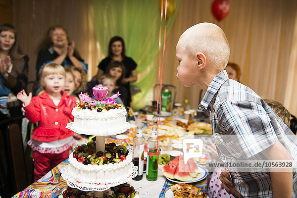 Kaukasischer Junge bläst Kerzen auf Geburtstagskuchen aus